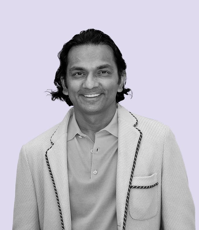 Black-and-white professional portrait of Div Turakhia, Founder of Media.net, smiling slightly, dressed in a formal blazer and white shirt against a subtle lavender background.
